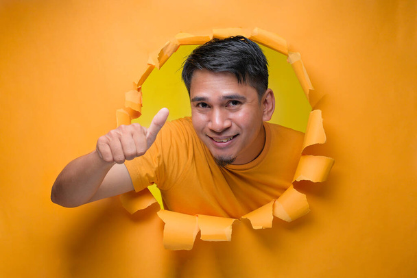 Młody, rozrywający człowieka przez rozdartą żółtą papierową dziurę ukazującą huk żartobliwej treści i szczęścia. Pojęcie zadowolenia z jakości i zalecenia - Zdjęcie, obraz