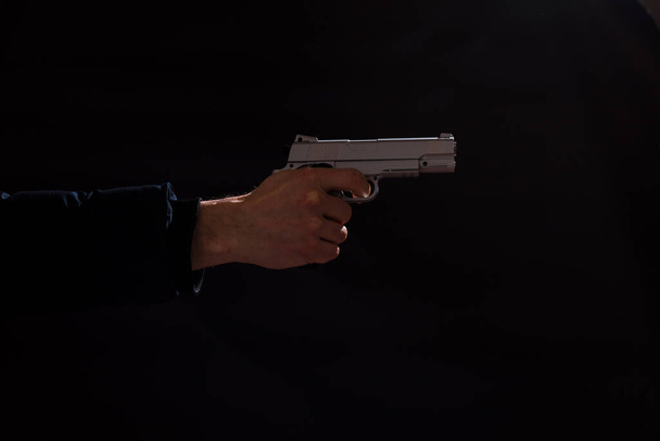 Die Hand des Mannes hält eine Waffe und zeigt darauf, auf schwarzem Hintergrund. - Foto, Bild