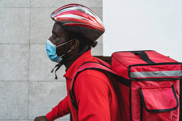 Afrykański jeździec dostarczanie posiłku do klientów z rowerów elektrycznych podczas noszenia maski twarzy podczas epidemii wirusa korony - Eco fast delivery food concept - Zdjęcie, obraz