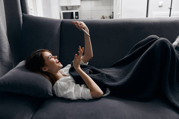 femme se trouve sur le canapé avec un téléphone dans sa main vue de côté confort intérieur - Photo, image