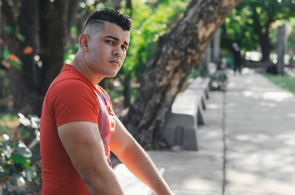 Modelo masculino de piel blanca de origen venezolano en la República Dominicana. sexy hombre en jeans en el parque al aire libre con naranja camina con luz natural entre las hojas sentadas en las escaleras - Foto, Imagen