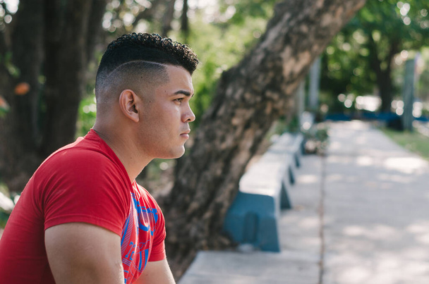 Modello maschile dalla pelle bianca di origine venezuelana nella Repubblica Dominicana. sexy uomo in jeans nel parco all'aperto con passeggiate arancioni con luce naturale tra le foglie seduti sulle scale - Foto, immagini