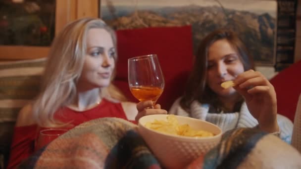若い女性はソファの上でリラックス毛布を飲みながらマルチワインと軽食を持っています - 映像、動画