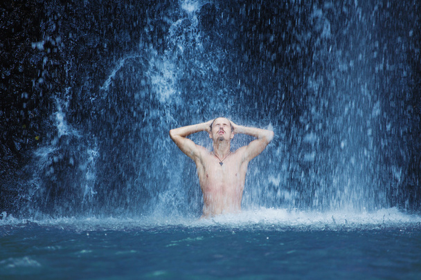 Young man refreshing in waterfall - Фото, изображение