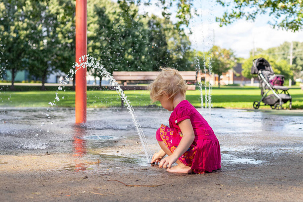 Μικρό κορίτσι παίζει με νερό splash pad και βρωμιά στο πάρκο την ηλιόλουστη μέρα του καλοκαιριού. - Φωτογραφία, εικόνα