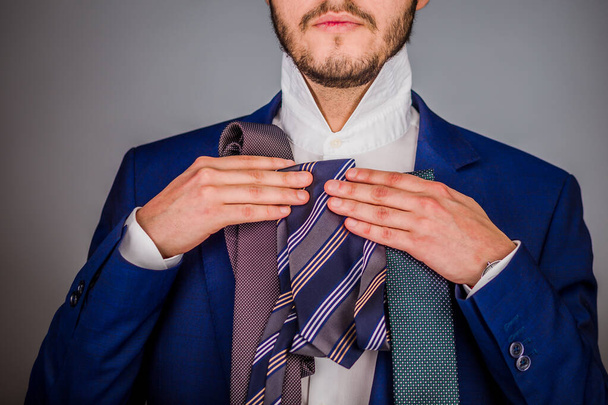 Молодой латиноамериканец выбирает стильный галстук. Изолированный элегантный человек выбрать галстук аксессуар для элегантного бизнеса. Концепция потребительской и модной одежды. - Фото, изображение