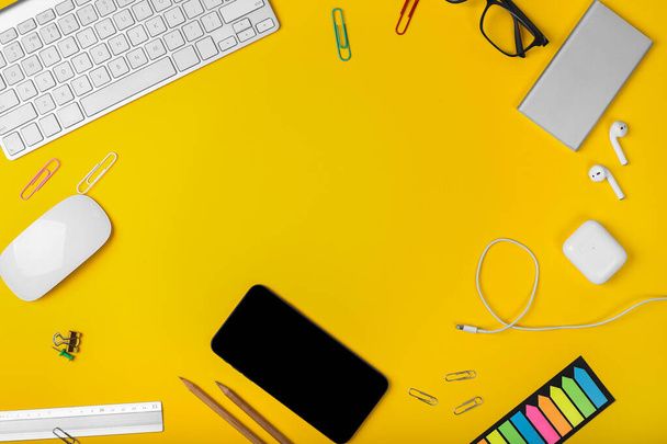 Mockup of smart gadgets on the background of office items on yellow background. Computer mouse and keyboard, headphones, smart watch and powerbank. Top view with copy space, flat lay. - Φωτογραφία, εικόνα
