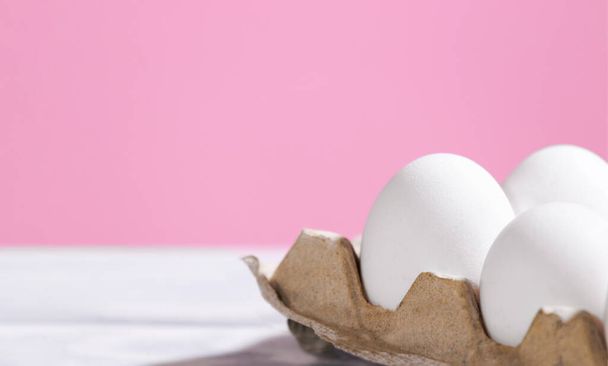 Uova di pollo bianco in una scatola di cartone su sfondo rosa, Uova fresche crude in un contenitore di carta, Prodotto Eko naturale, Copyspace, Sfondo alla moda - Foto, immagini