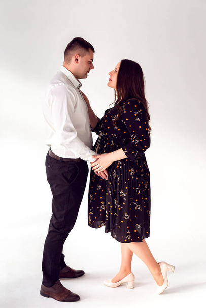 Man en zwangere vrouw op een witte achtergrond. Guy houdt zwanger meisje buik liefde relatie wit achtergrond - Foto, afbeelding