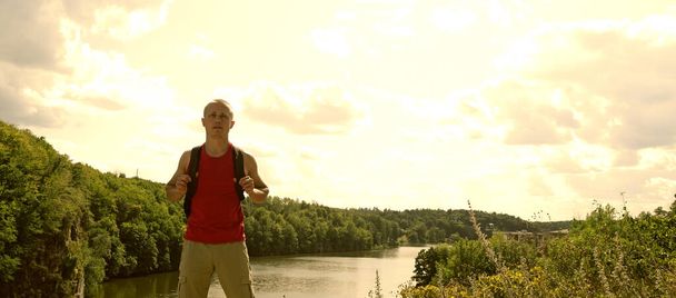 Un joven deportista se encuentra sobre el río y el bosque. Turismo fuera de la ciudad - Foto, imagen