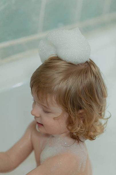 close up portrait of a child in a bath with foam on blond curly hair - Photo, Image