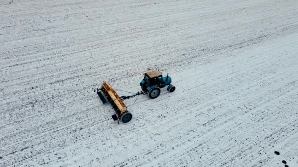 Kino rolnika na ciągniku z agregatem rolniczym uprawia pole w zimie i dodaje nawozy do śnieżnej gleby - Materiał filmowy, wideo