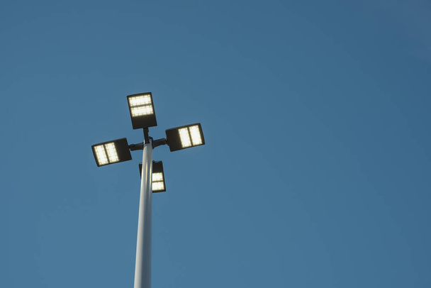 Uma visão olhando diretamente para as luzes de rua de baixo mostra o poste e luminária contra um céu azul sólido. - Foto, Imagem