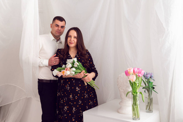 Liefde en relaties. Paar op een achtergrond van witte luchtige stof Meisje met een boeket tulpen op een witte achtergrond met plaats voor tekst. - Foto, afbeelding