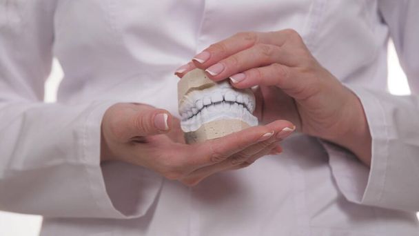 Bir ortadont 'un ellerinde alçıdan yapılmış çarpık dişlerden oluşan beyaz bir çene. Çocuk ve yetişkinlerde ısırık düzeltmesi üzerine sunum yapan bir dişçinin yakın çekimi. Hastanelerde klinik deneyler - Fotoğraf, Görsel