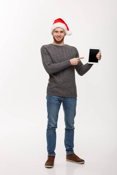 Urlaubs- und Geschäftskonzept - Junger gutaussehender Mann zeigt Tablet-Bildschirm und zeigt mit dem Zeigefinger. - Foto, Bild