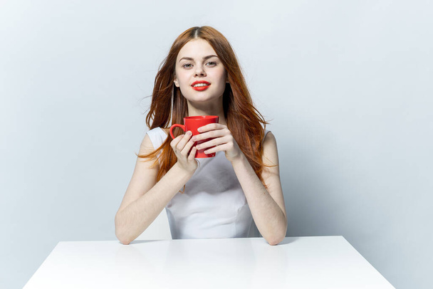 Hübsche Frau am Tisch mit rotem Becher in der Hand  - Foto, Bild
