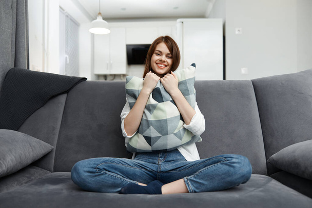 mujer alegre con una almohada en las manos se sienta en el interior del apartamento sofá de descanso - Foto, Imagen