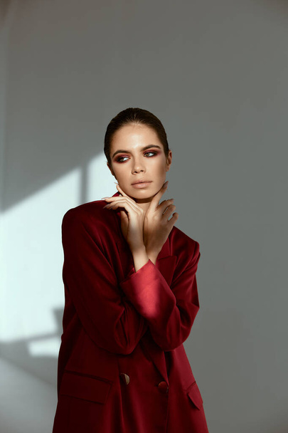 brunetka z jasny makijaż trzyma ręce w pobliżu twarz glamour modne ubrania czerwona kurtka - Zdjęcie, obraz