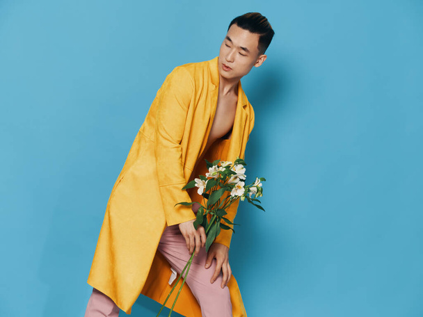 Attractive Asian man in a yellow coat and pink trousers with a bouquet of flowers in his hand - 写真・画像