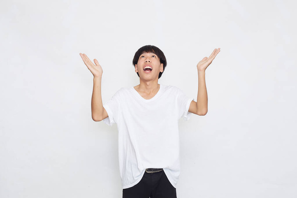 Opgewonden verrast schattig jong aziatisch man in casual wit t-shirt doen open hand gebaar op grijze achtergrond - Foto, afbeelding