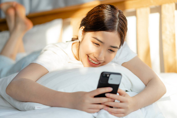 mooie aziatische vrouw met behulp van haar telefoon wanneer ze net wakker - Foto, afbeelding