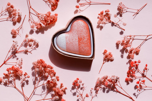 Ένα κουτί συμπαγούς σκόνης σε σχήμα καρδιάς σε ροζ χάρτινο φόντο με γυψόφυλλες. Στο πάνω μέρος. Καλλυντικό για μάγουλα. Ψημένο τριχρωμία - Φωτογραφία, εικόνα