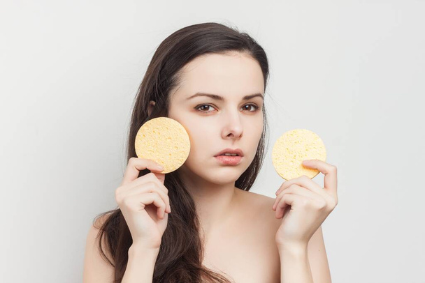 pretty brunette naked shoulders wipes her face but clean skin with a sponge - Photo, Image