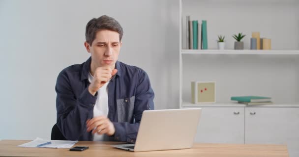 Figyelmes szabadúszó Y-generációs srác üzletember gondolkodik online szolgáltatás probléma laptop. Súlyos kétes férfi ül otthon office desk figyelembe véve a pénzügyi kockázatok, hogy nehéz döntés - Felvétel, videó