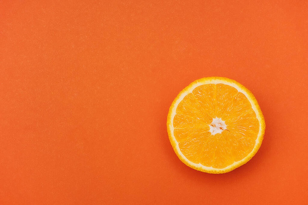 Una sola rebanada de una naranja sobre un fondo naranja. Esquina de la foto. Copiar espacio. Espacio vacío. - Foto, imagen
