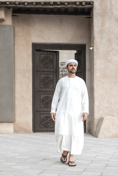 Dubai 'nin tarihi Shindagha bölgesinde geleneksel giysiler içinde Arap bir adam kapıdan çıkıyor. - Fotoğraf, Görsel