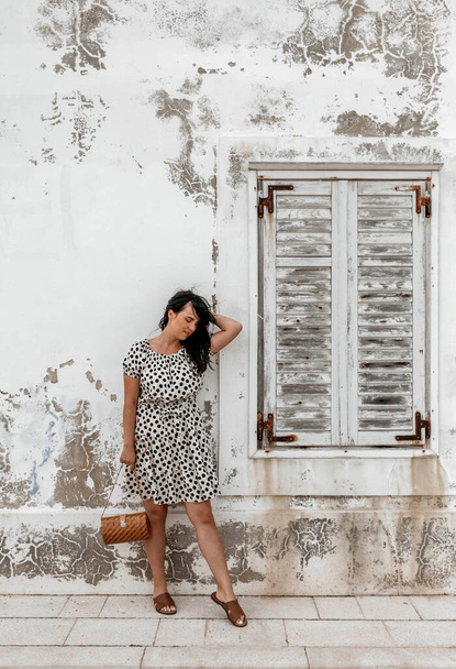 A vertical shot of a caucasian brunette female standing in front of the window on a white grunge wall - Fotografie, Obrázek