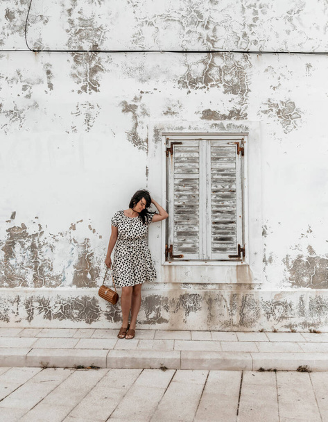 A vertical shot of a caucasian brunette female standing in front of the window on a white grunge wall - 写真・画像