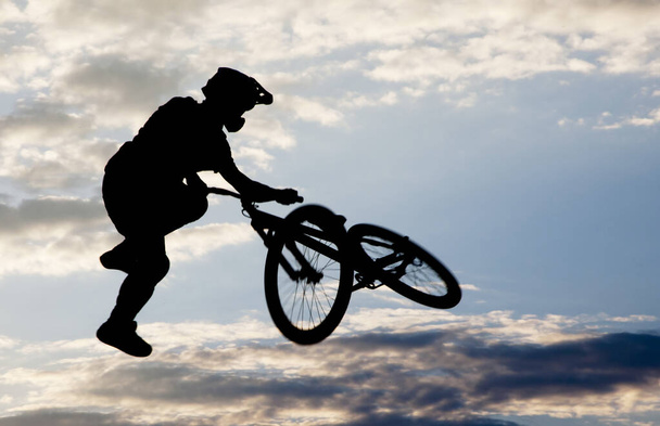Gün batımında bisikletle atlayan bir adamın silueti. - Fotoğraf, Görsel