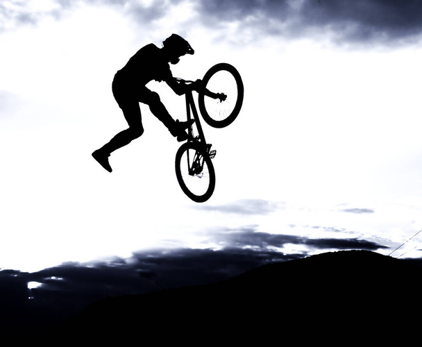 日没の空に対して自転車でジャンプを行う男のシルエット - 写真・画像