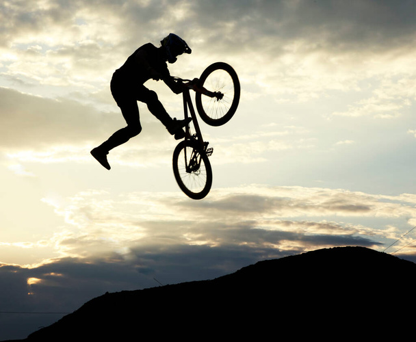 Silhouette d'un homme faisant un saut avec un vélo contre le ciel couchant - Photo, image