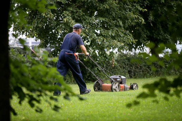Чоловік повернувся, порізавши траву червоною косаркою. Садівництво та ландшафтний дизайн. 08 17 2017 року
 - Фото, зображення