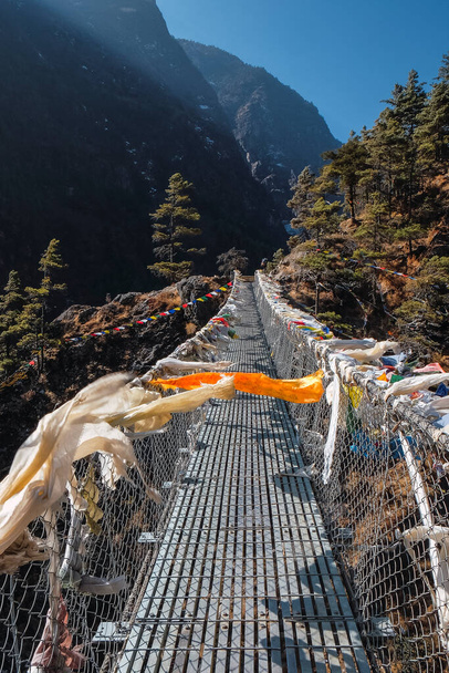 Coloridas banderas de oración budistas ondeando en el viento en el popular puente colgante Hillary en el camino a Namche Bazar en el Himalaya, Nepal, en el campamento base del Everest. - Foto, Imagen