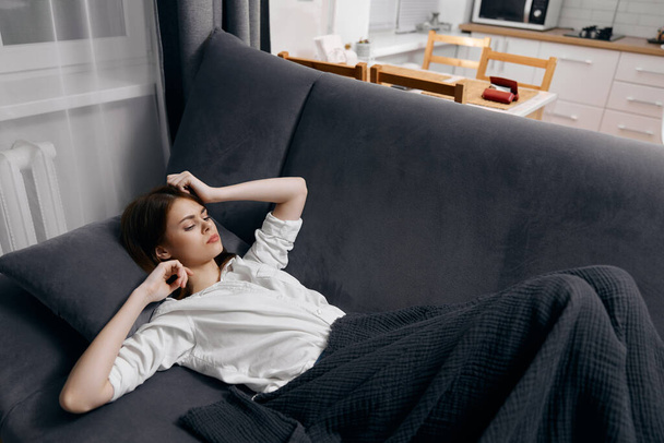 a woman in a white t-shirt lies on the sofa under a blanket and gestures with her hands - Foto, afbeelding