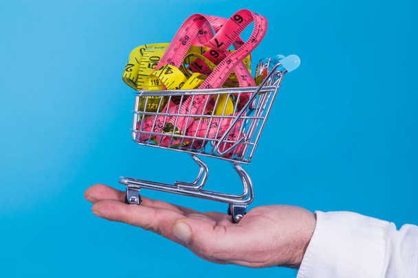 hand holding miniature supermarket cart full of tape measures, diet and slimming concept - Fotó, kép