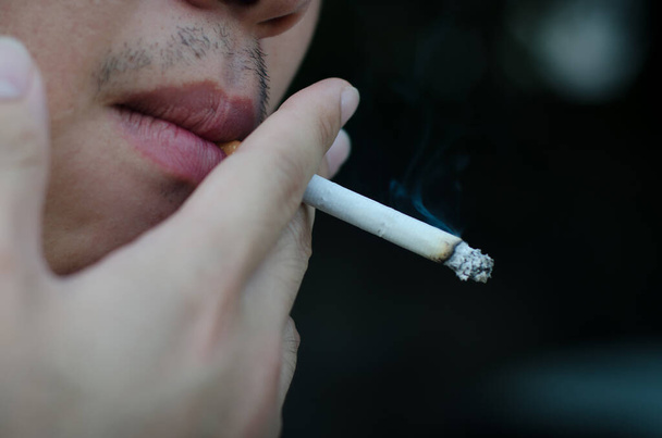 joven hombre fumando cigarrillo sobre fondo negro - Foto, Imagen