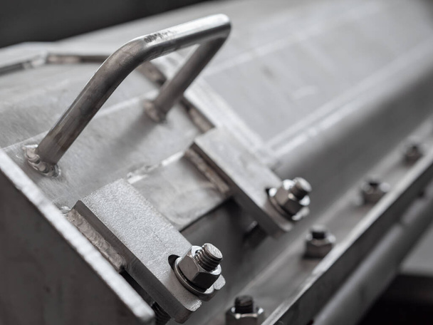 Closeup of hatch and handle of enclosed screw conveyor made from stainless steel. Shallow depth of field with the bolt in the foreground in focus. - Photo, Image