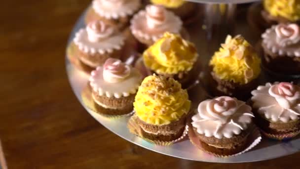 Stand con cupcake decorati con crema gialla e rosa in un banchetto festivo  - Filmati, video
