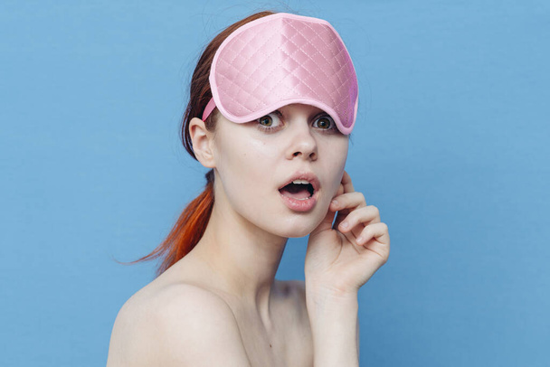 mulher alegre com uma máscara médica na cabeça em um fundo azul olha para o lado - Foto, Imagem