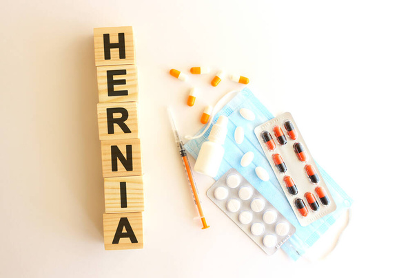 Le mot HERNIA est fait de cubes en bois sur fond blanc avec des médicaments et un masque médicaux. - Photo, image