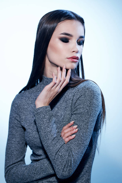 Hermosa mujer en un suéter gris gestos con sus manos y maquillaje con sombra de ojos en los párpados - Foto, Imagen