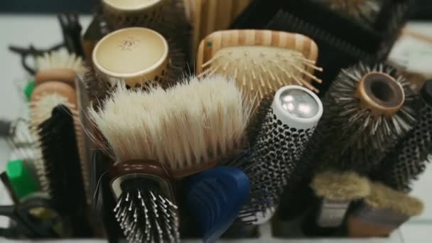 Muchos peines de diferentes cabellos y materiales se colocan en un soporte en la mesa cerca del espejo de un peluquero en un salón de belleza - Imágenes, Vídeo