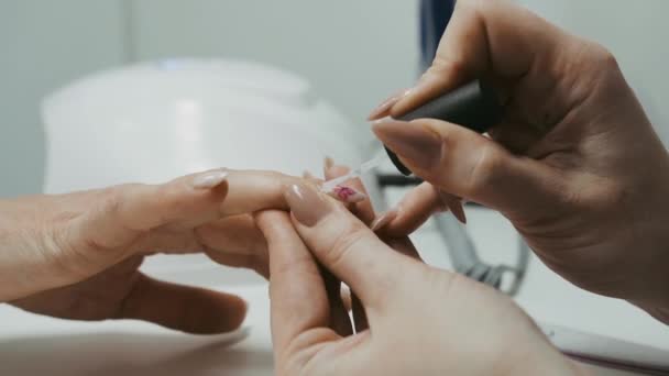 En el salón de belleza, la manicura cubre las uñas del cliente con un acabado de barniz. Primer plano - Metraje, vídeo