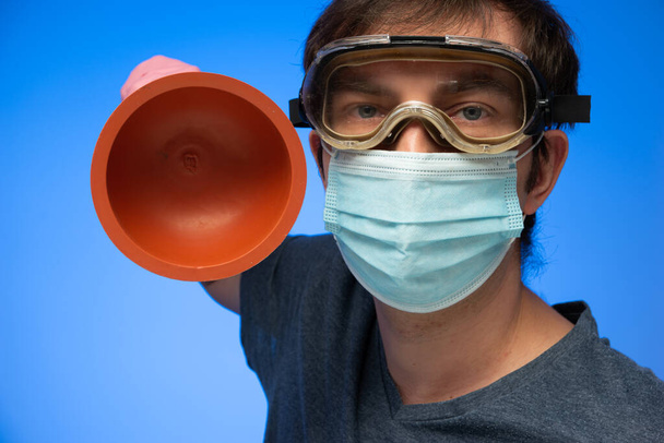 Drain hole plunger held in hand by Caucasian male with protection goggles and face mask making expressive gesture close up studio shot. - Photo, Image
