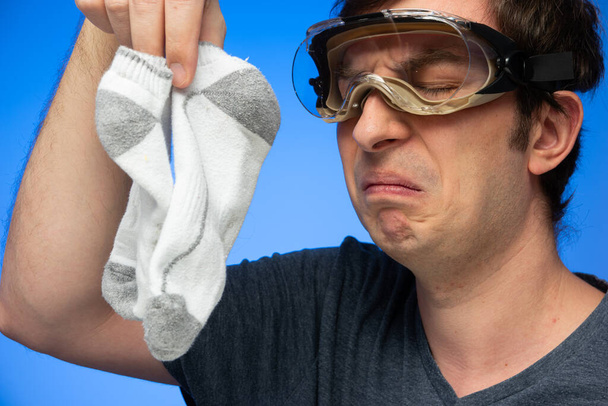 Blanke man draagt bril maakt walgelijk gezicht gebaar op stinkende witte sokken in de hand gehouden studio schot. - Foto, afbeelding